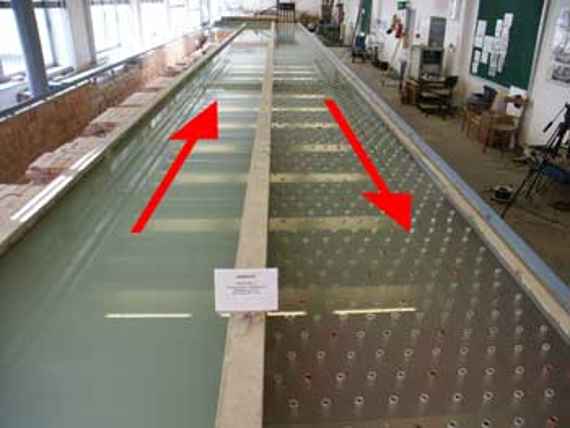 Man sieht die 2 40 Meter langen und 1,5 Meter breiten Rinnen des Modellversuchs. In der links Rinne ist nur Wasser. In der rechten Rinne simulieren graue Kunststoffrohre die Wasserpflanzen.