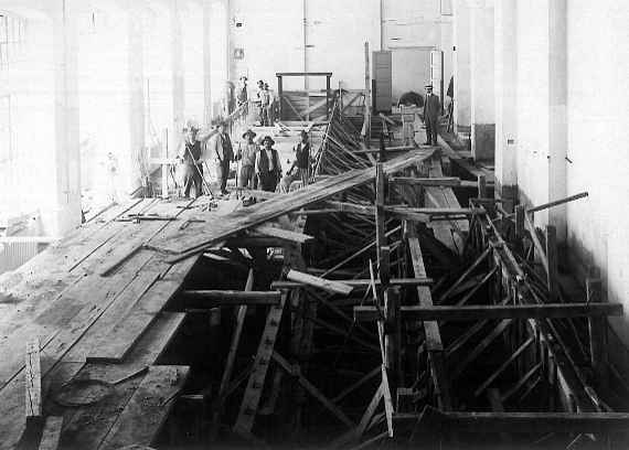 Overview of the construction site - two half-built model tanks and construction workers with hats.