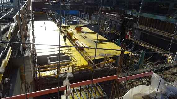 Construction in the basement area is progressing, there are wooden boards on top and two construction workers.