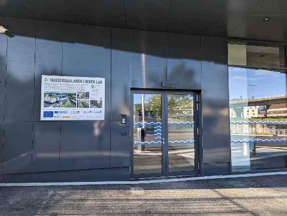 The picture shows the side entrance with intercom in case the main entrance is closed. The main entrance is further to the right, outside the photo. To the left of the entrance is a sign for the hydraulic engineering laboratory. The text is described in the following picture.