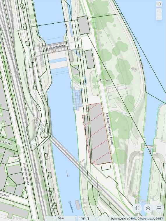 The screenshot shows the new building in grey on a map. The Danube Canal runs on the left, the actual Danube a little further away on the right, with the lock for ships between the Danube and the Danube Canal clearly visible. Green areas show areas with meadow, trees and bushes. Grey lines mark railway lines.