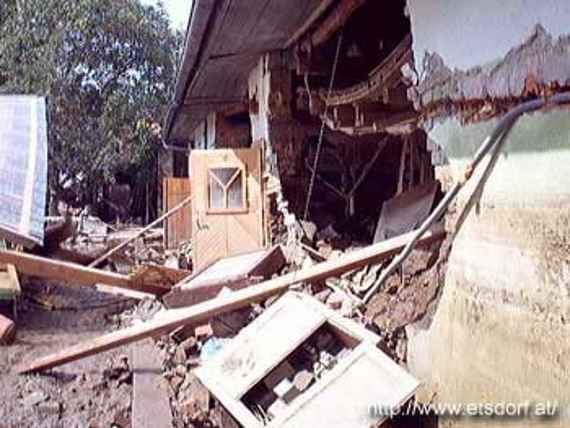 Damaged houses in the village of Kamp, you can see a house where an outer wall has collapsed, bricks and boards lie around, cables are torn out of the wall and hang loose.