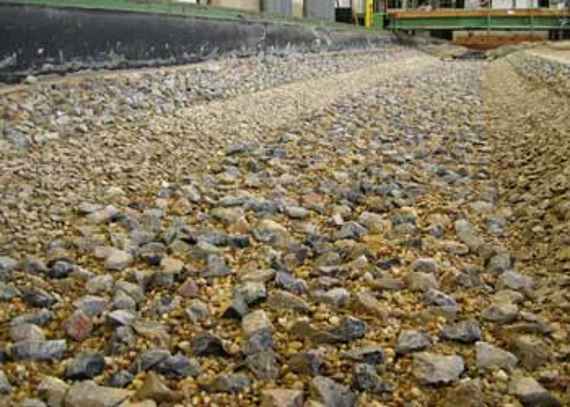 Open armour layer in model test. Individual larger stones lie on a riverbed of coarse sand.