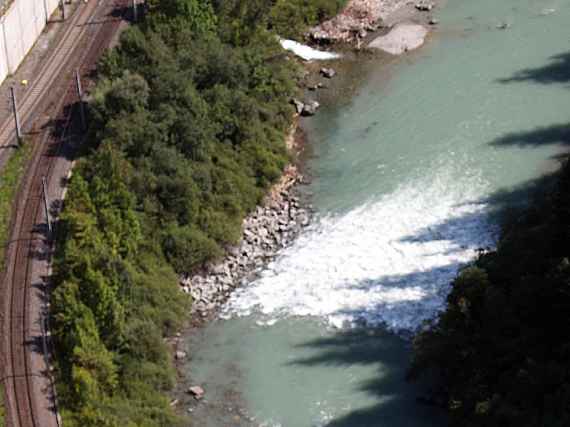 The photo shows one of the ramps developed in the model test, which stabilize the river bed of the Salzach and thus protect the parallel running railway line from erosion. You can see the railway line. The water flows faster over the ramp and is coloured white by the air mixed in.