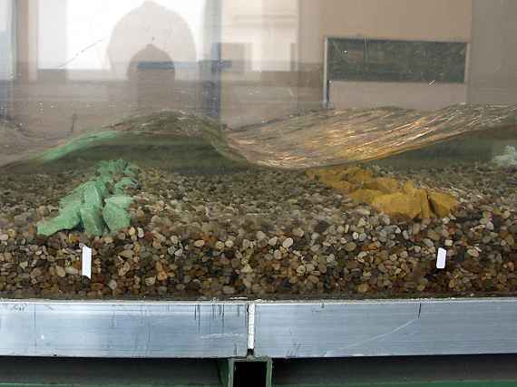 In a model hydraulic engineering experiment, large stones lie on a riverbed and water flows over them.