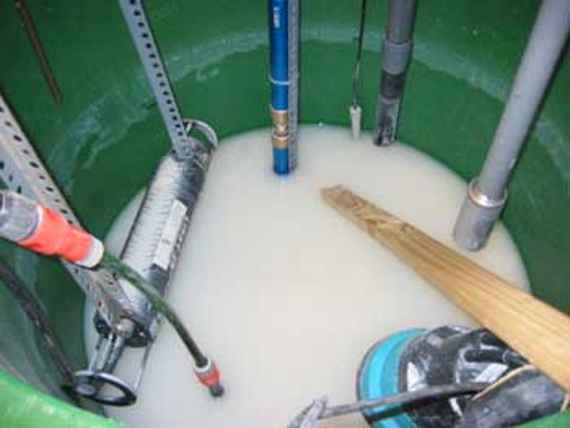 Container with the four measuring instruments, the submersible pump and additionally a wooden rod for stirring up suspended solids lying on the ground. The container is being filled with water via a hose.