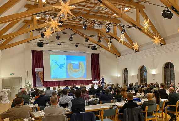 You can see the participants sitting at the back of the fishing conference at Mondsee Castle. On the stage is a large screen on which a presentation is being shown.