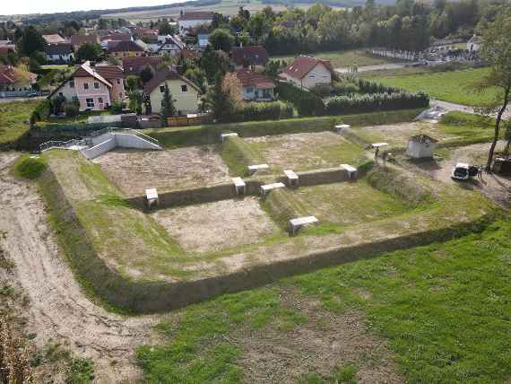 Aerial view of the research basin in Breitenwaida. The basin is divided into five smaller segments by earth walls. Behind it are some houses, in front of it meadow.