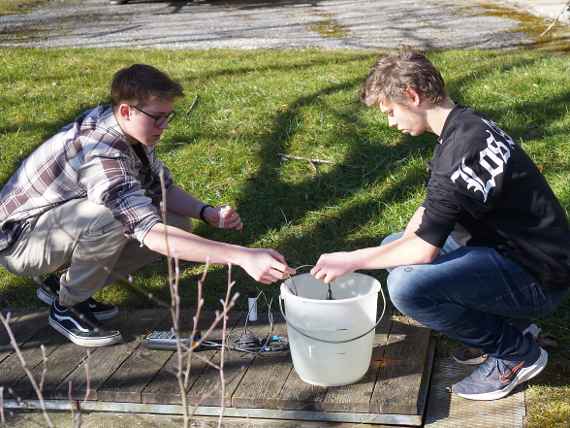 Zwei Schüler bei der Messung der wasserchemischen Parameter im Teich mit einem Messgerät im Kübel.