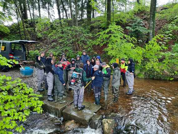 Die Teilnehmerinnen und Teilnehmer stehen am Bach.