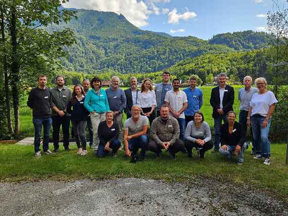 Gruppenfoto der Teilnehmer:innen am SIL-Austria Meeting 2025. Im Hintergrund sieht man Bäume und einen Berg.