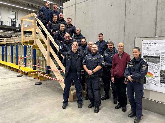 Ein Gruppenbild mit 15 Polizistinnen und Polizisten sowie dem Leiter des Instituts für Wasserbau und hydrometrische Prüfung, die auf einer Treppe aus Holz stehen.