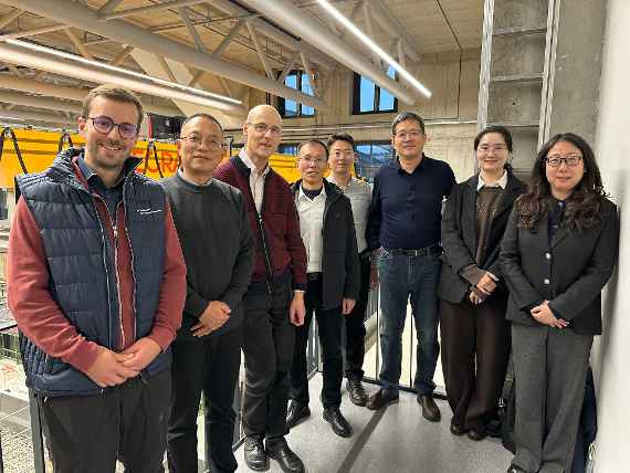 Acht Personen stehen auf einer Galerie und Blicken zum Fotoapparat. Im Hintergrund sieht man eine große Halle.