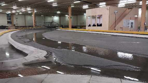 In einer großen Halle ist das Modell eines Flusses aufgebaut. Zwischen zwei Wänden ist der Fluss mit Sand modelliert. In der Tiefenrinne des Sandbetts fließt Wasser.