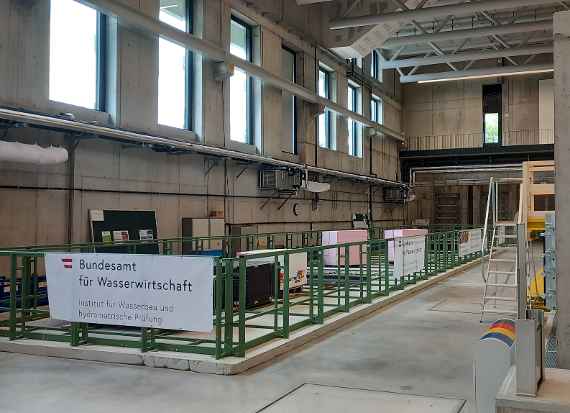 Die im Aufbau befindliche Flussbaurinne des Instituts für Wasserbau und hydrometrische Prüfung: Stahlelemente, die den statischen Rahmen der Rinne bilden, stehen auf einem Betonfundament. Weiteres Baumaterial steht im inneren der Stahlbegrenzung.