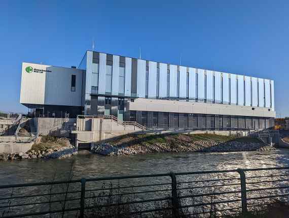 Gerader Blick zum Neubau über den Donaukanal, aufgenommen unterhalb der Autobahn. Es sind das Logo „BOKU“ sowie die Beschriftungen „Wasserbaulabor“ und „River Lab“ zu lesen. Bei den Treppen sind noch provisorische Geländer zu sehen, welche demnächst verschwinden.