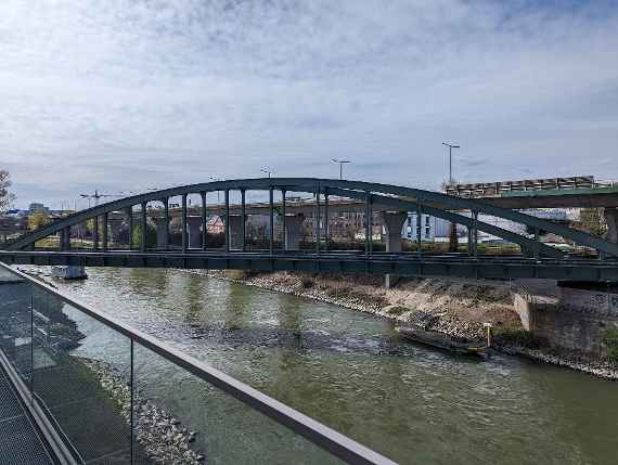 Schräger Blick aus dem Hauptgebäude nach links. Auf dem Donaukanal sind zwei Bootsstege am Land befestigt, eines vor und eines nach der Eisenbahnbrücke. Dahinter schräg verlaufend die Autobahnbrücke und einige Wohnhäuser. Fast ganz links hinten erkennt man das Allgemeine Krankenhaus.