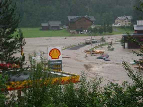 Überflutete Straße durch Hochwasser, vorne eine Tankstelle, weiter hinten einige Häuser, welche nicht überflutet wurden.