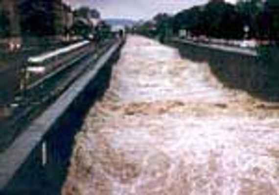 Wienfluss in Wien bei Hochwasser mit großen Wellen, daneben fährt eine U-Bahn, nur durch eine Mauer vom reißenden Fluss getrennt.
