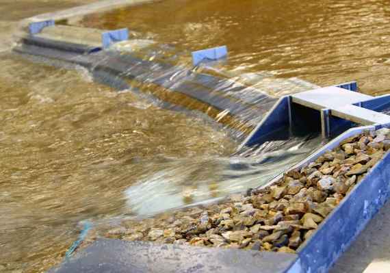 Hochwasserschutz Wehranlage im Modellbau, Foto etwas schräg aufgenommen; Wasser fließt von rechts nach links über die Wehranlage.