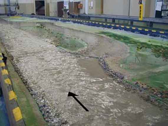 Physikalisches Modell beim Bemessungsabfluss hundertjährlichem Hochwasser (Q = 762 Kubikmeter in Sekunde), man sieht einen Blick auf das physikalische Modell bei einem einhundertjährlichen Hochwasser. Der Großteil des Durchflusses führt über den linksseitigen Gewässerarm, das heißt durch die Geschiebefalle, und nur ein kleiner Teil durch das Umgehungsgerinne.