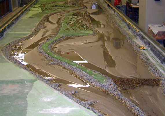 Physikalisches Modell des Lech nahe Reutte, man sieht einen Fluss in einer Laborrinne gebaut aus Sand und Steinen, die Grünflächen entlang des Flusses sind betoniert und grün gestrichen.
