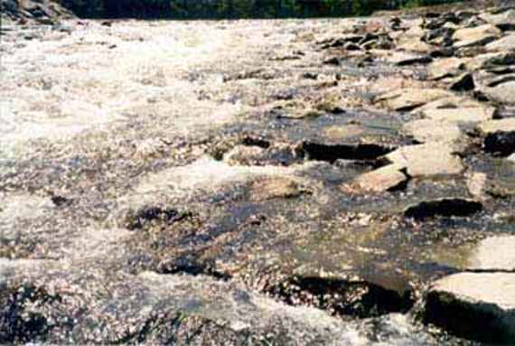 Strömung über die Blocksteinrampe, man sieht ein mit großen Wasserbausteinen ausgelegtes Gewässerprofil. Darüber fließt eine geringe Wassermenge.