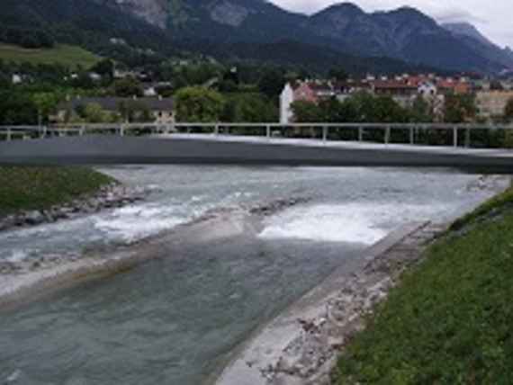 Bild zeigt den Fluss Sill, im Hintergrund eine Brücke, dahinter einige Häuser und ganz hinten Berge.