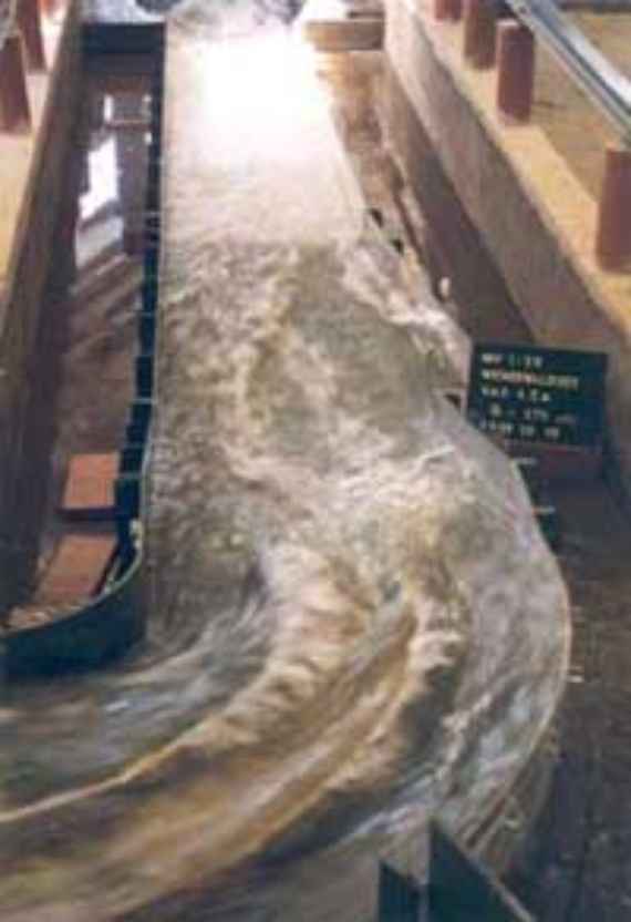 Hochwasserabfluss in der Schussrinne mit hochgezogener Prallwand an der Außenkurve, man sieht die Hochwasserentlastungsrinne beim Bemessungsabfluss mit hochgezogener Wand am Außenufer in der Kurve.