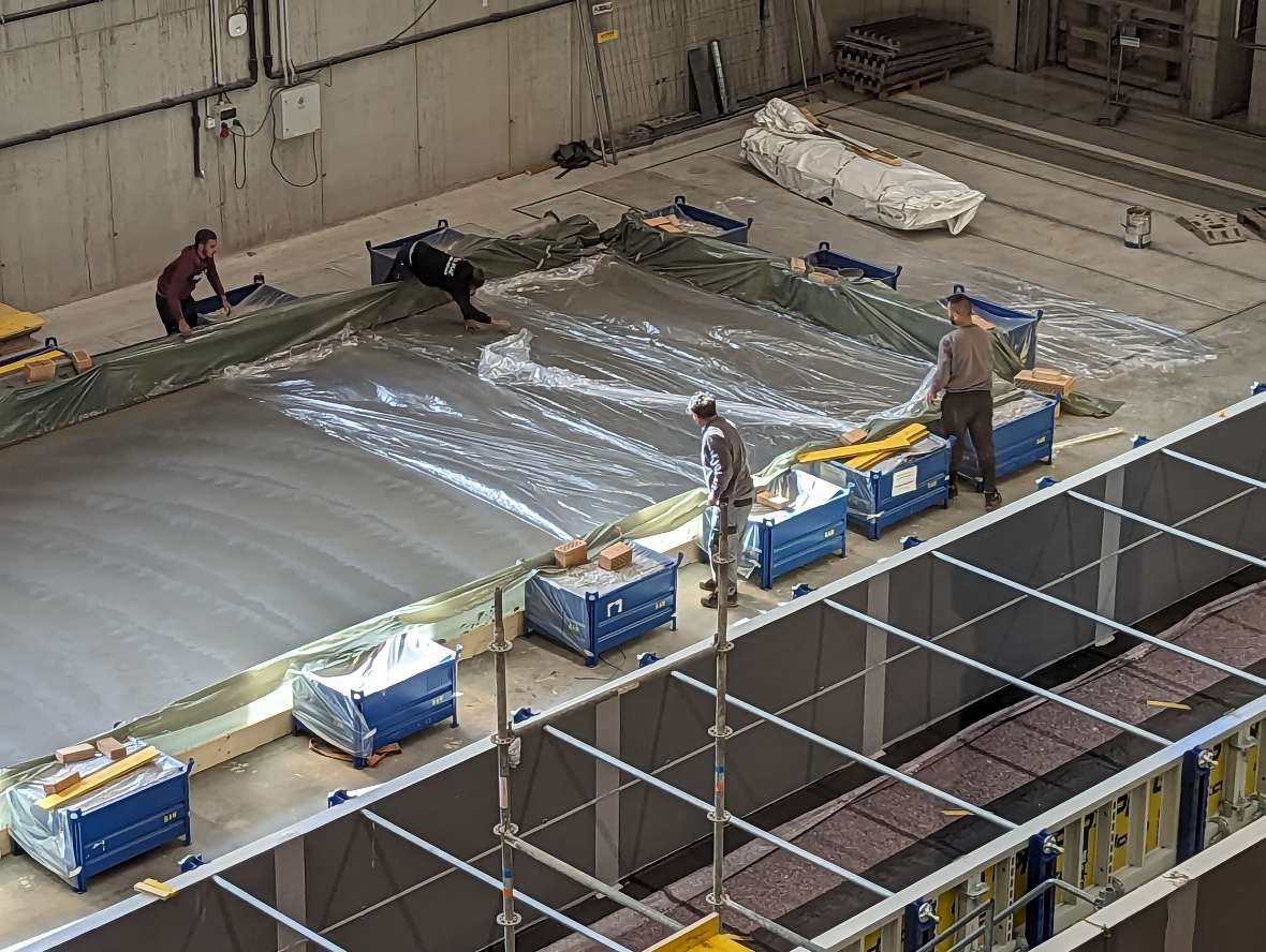 Four people cover the finished smoothed concrete with a plastic sheet to prevent it from drying out too quickly.