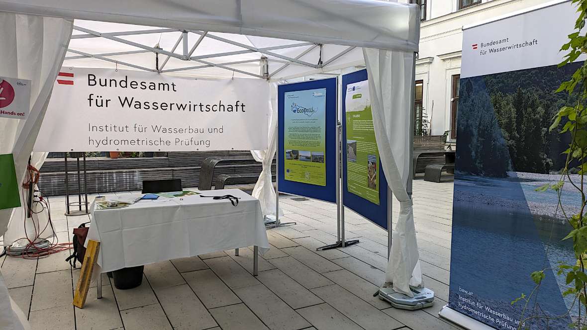 The photo shows the right side of our information stand on an outdoor terrace. In front is a table with information material, to the right of it 2 large boards with posters about our projects. The table and posters are protected by a party tent.