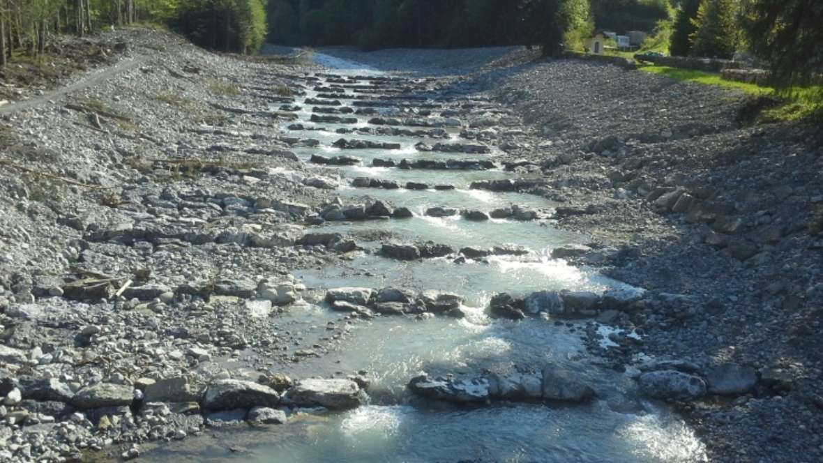 In the renatured river, water flows over large and small stones.