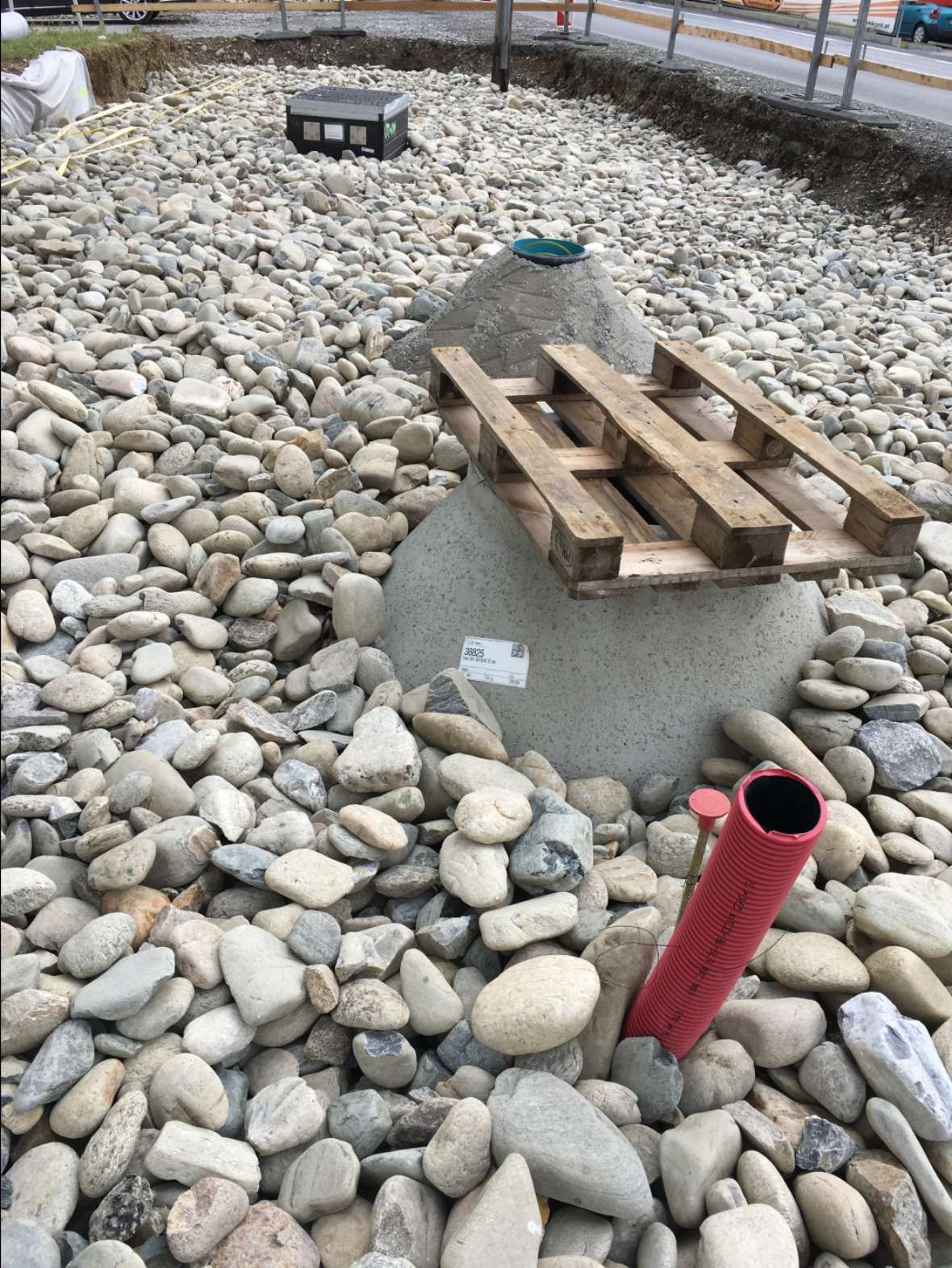 The picture shows the structural substrate of the Gradnerstrasse test facility in Graz. In the very front a red pipe, behind it 2 concrete blocks. The soil is covered with approximal 5 to 20 cm stones.