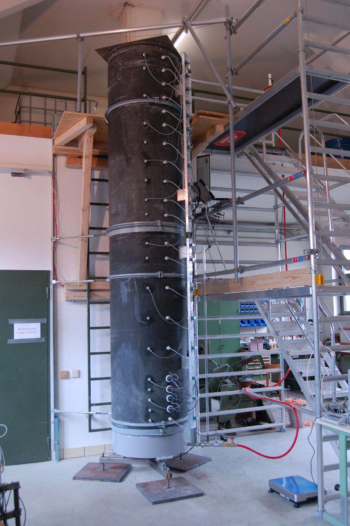 Here the picture shows a finished indoor lysimeter from the outside. Next to it is a scaffold with stairs to reach the top of the 4 m high cylinder. On the left you can see a door.