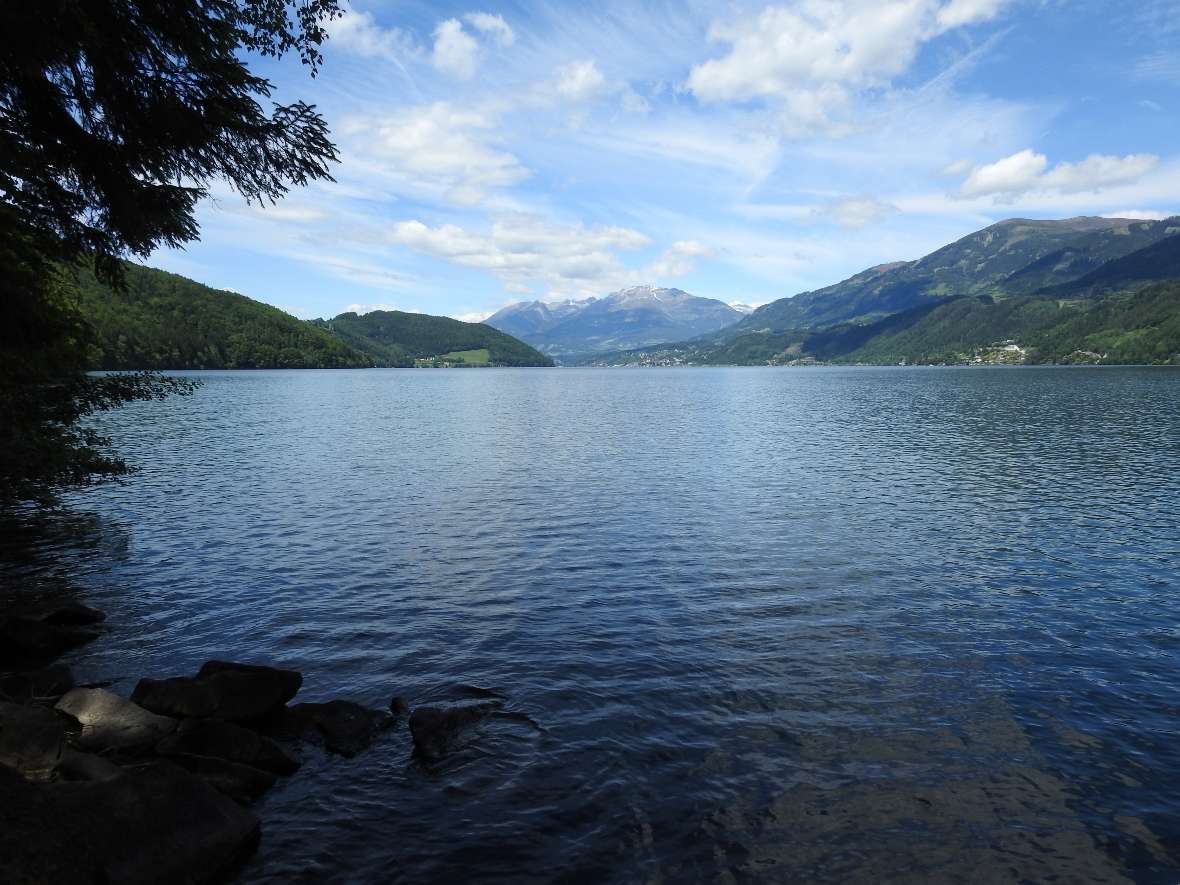 Das Foto zeigt einen großen See in Österreich, eingefasst von bewaldeten Hügeln und kleineren Siedlungen, ganz im Hintergrund in der Mitte ist ein hoher Berg zu sehen. Die Erfassung der Fischgemeinschaft eines großen Sees erfordert hohen Personal- und Arbeitseinsatz. eDNA-Methoden können hier in Zukunft evtl. unterstützend eingesetzt werden