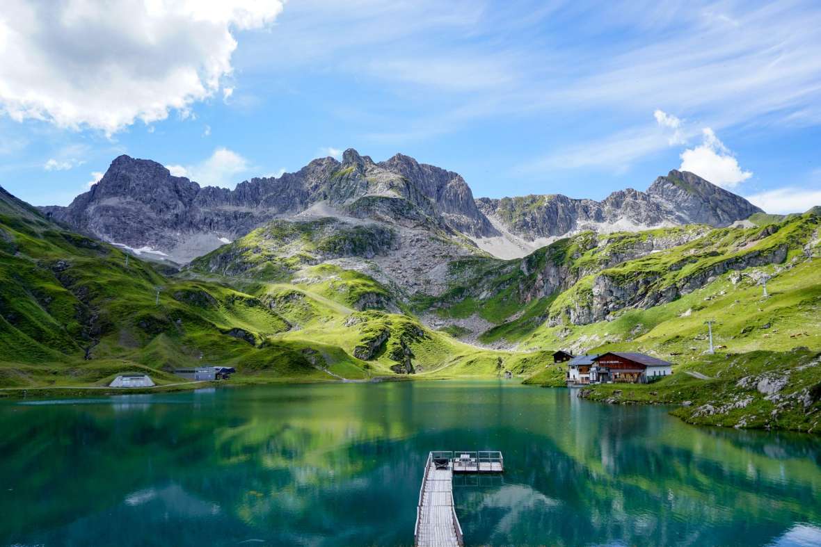 Jury Platz 4: Die Alpen spiegeln sich im Zürersee. Neben dem See befindet sich eine Almhütte und ein kleiner Steg führt ins Wasser.