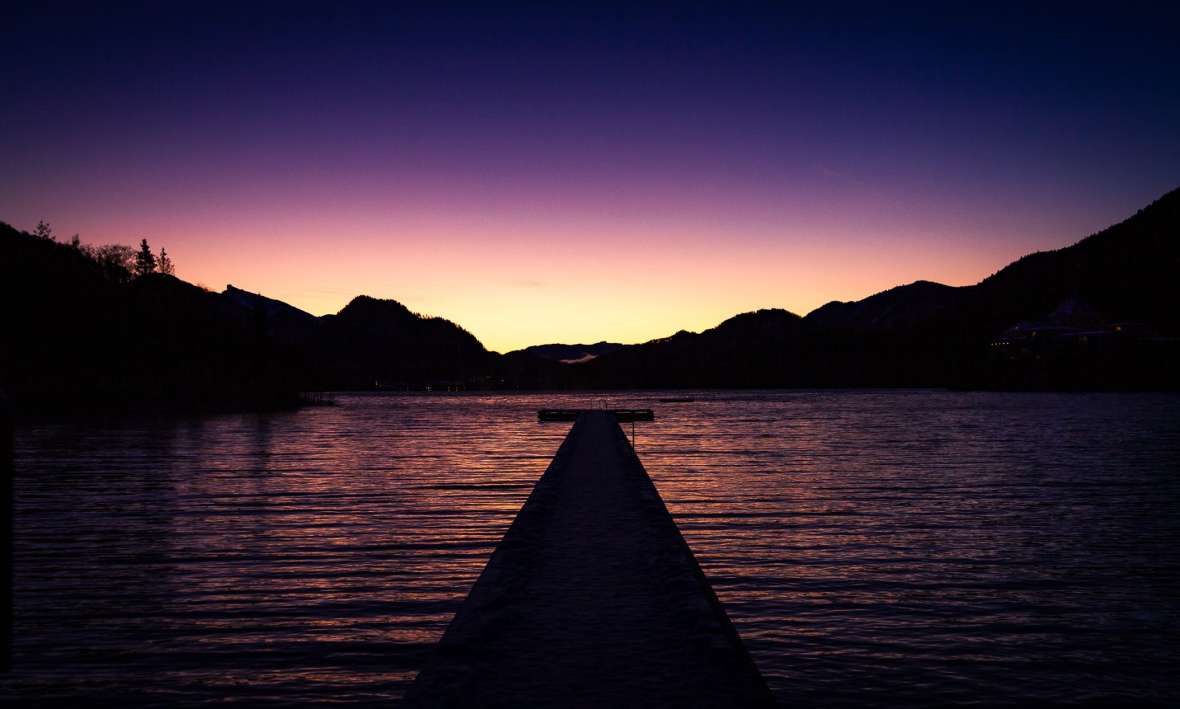 Puplikum Platz 5: Steg führt auf den ruhigen Fuschlsee, umgeben von dunklen Bergen, unter farbigem Abendhimmel mit Verlauf von Orange zu Violett.