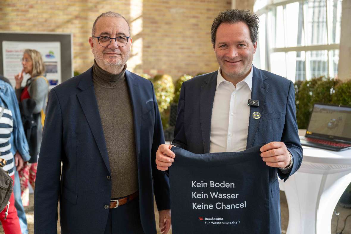 BAW-Direktor Peter Strauss und BM Norbert Totschnig im Palmenhaus. BM Norbert Totschnig hält den Stoffbeutel mit der Aufschrift "Kein Boden, kein Wasser, keine Chance" in der Hand. 