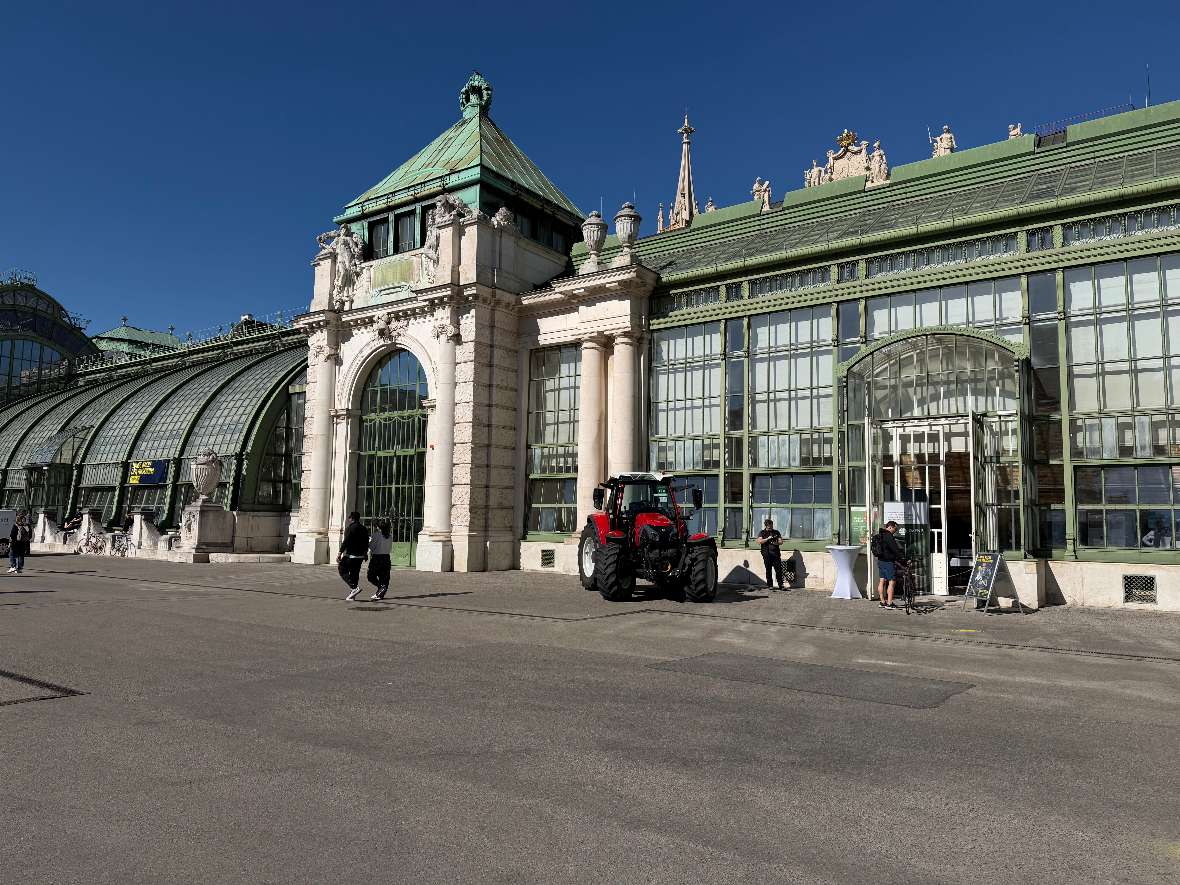 Außenansicht Palmenhaus Wien mit einem Traktor davor.