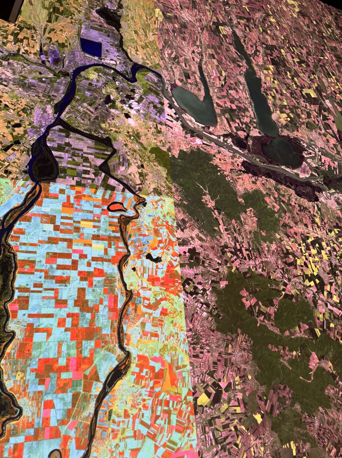 Luftaufnahme einer Landschaft mit Fluss, Seen und landwirtschaftlichen Feldern in verschiedenen Farben.