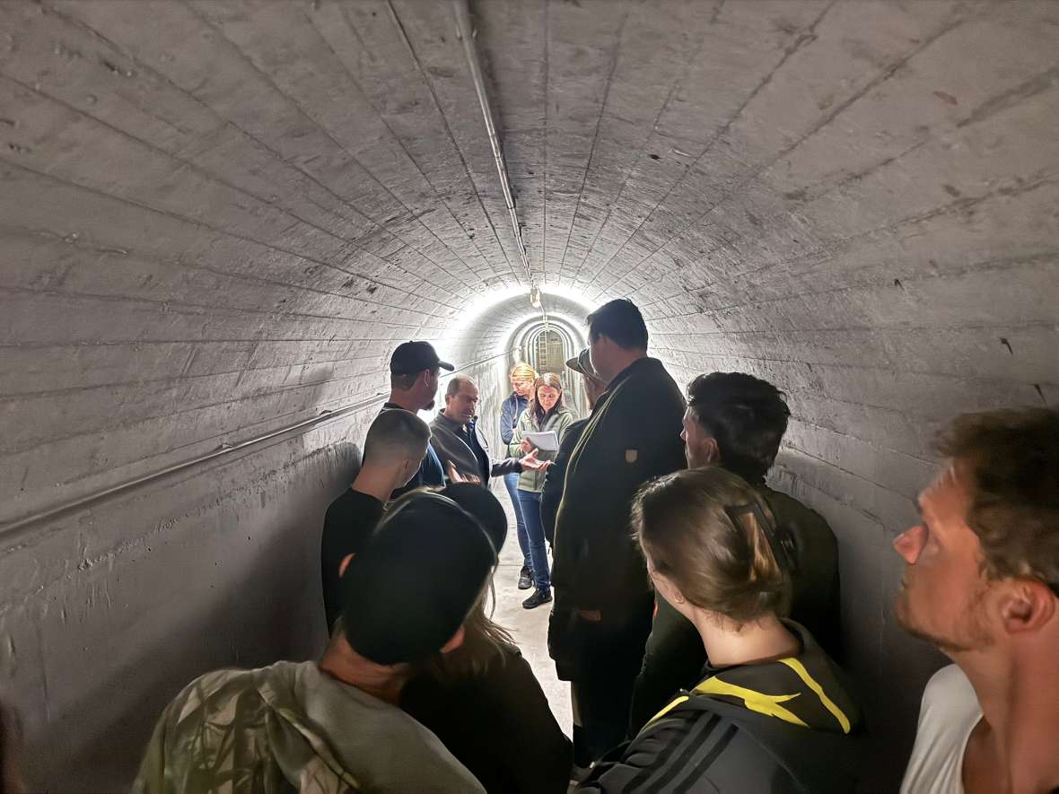 Die Gruppe steht im Kraftwerk Bischofshofen in einem gewölbten Tunnel mit markanten Betonwänden.