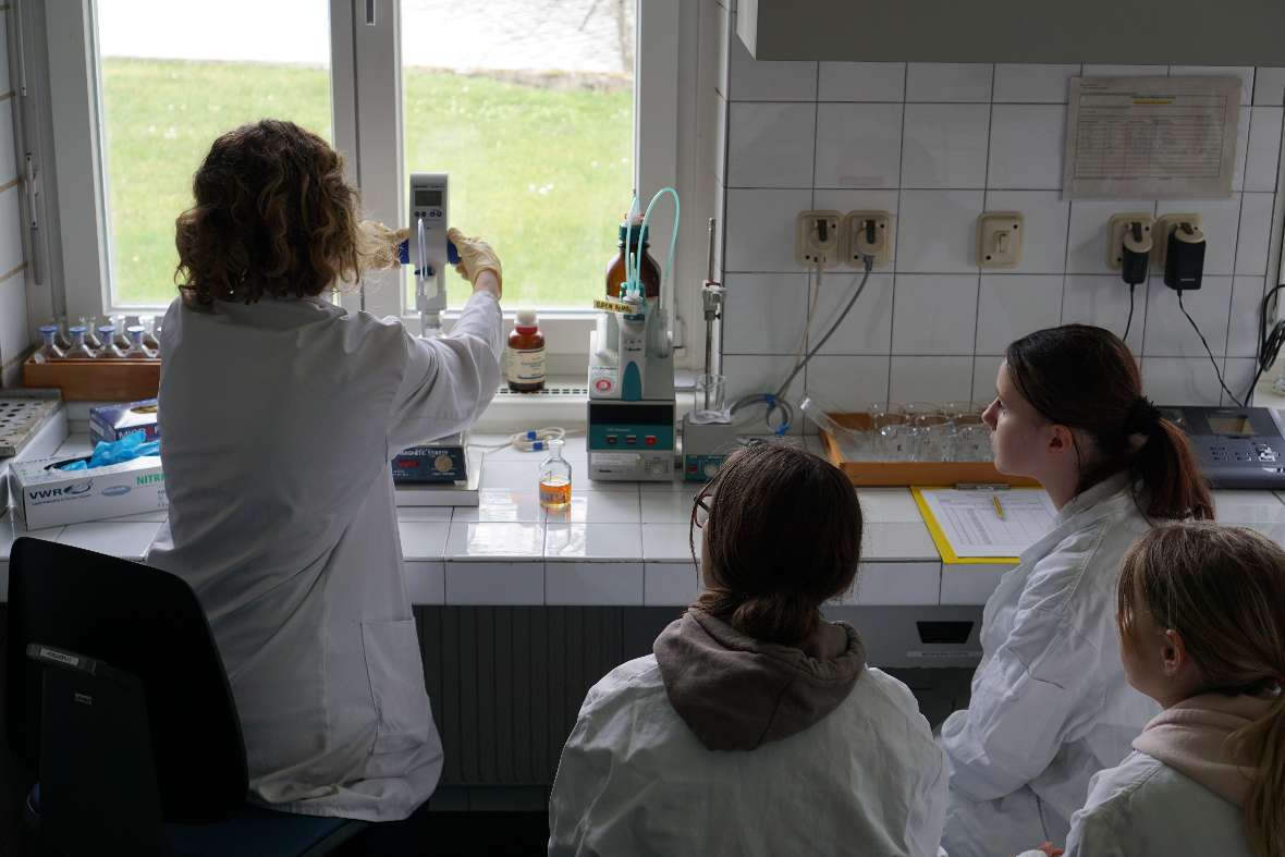 Mitarbeiterin zeigt Schülerinnen etwas im Labor am Mikroskop
