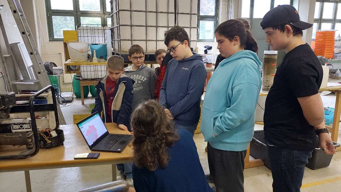 Eine Mitarbeiterin zeigt den Schülerinnen und Schüler im Labor eine Abbilung am Laptop. 
