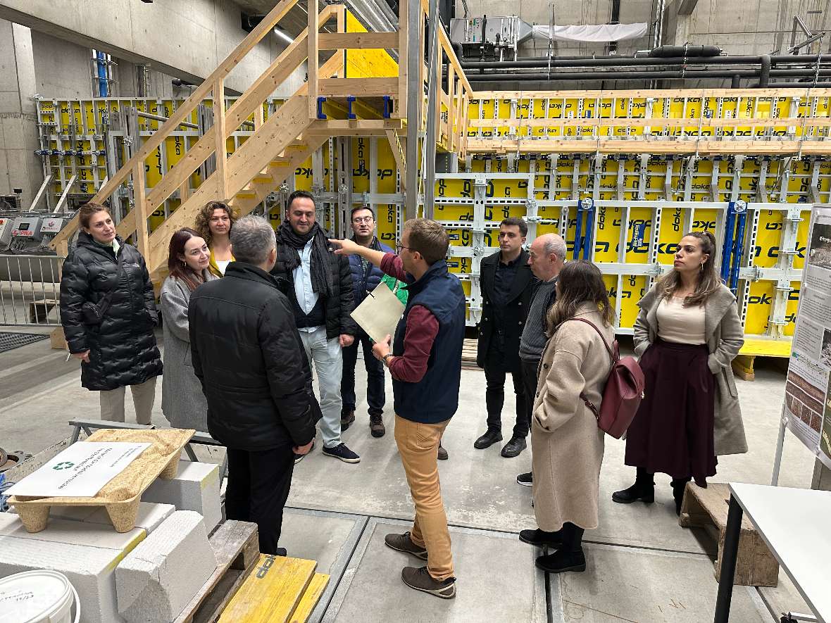 © Die Mitarbeiter:innen der türkischen Ministerien stehen in einer Versuchshalle des Wasserbaulabors und hören gespannt unserem BAW-Mitarbeiter Martin Hasenhündl, der durch das Haus führt, zu.