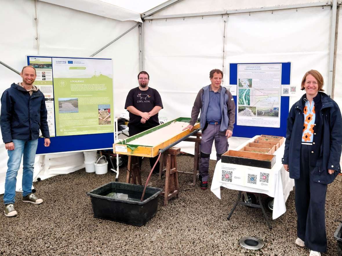 Die Mitmach-Station besteht aus zwei Experimentier-Rinnen und einigen Postern über das Localience-Projekt. Davor steht das betreuende Team.