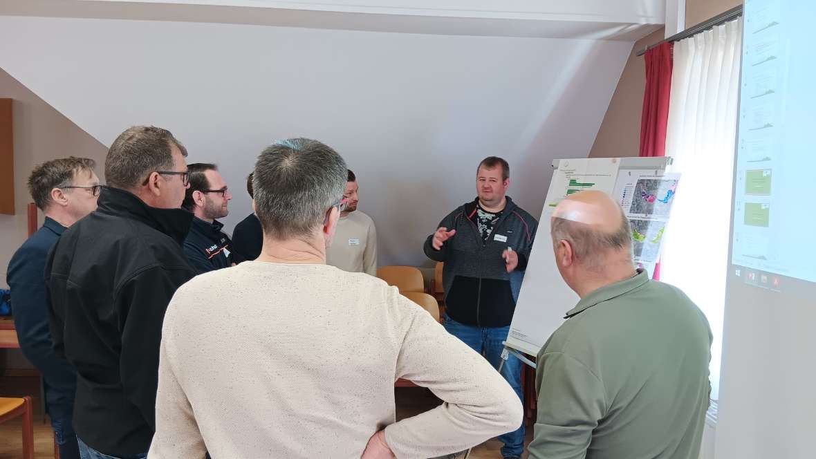 Eine kleine Gruppe von Teilnehmenden steht um einen Posterständer herum und diskutiert eine Frage aus dem Workshop.