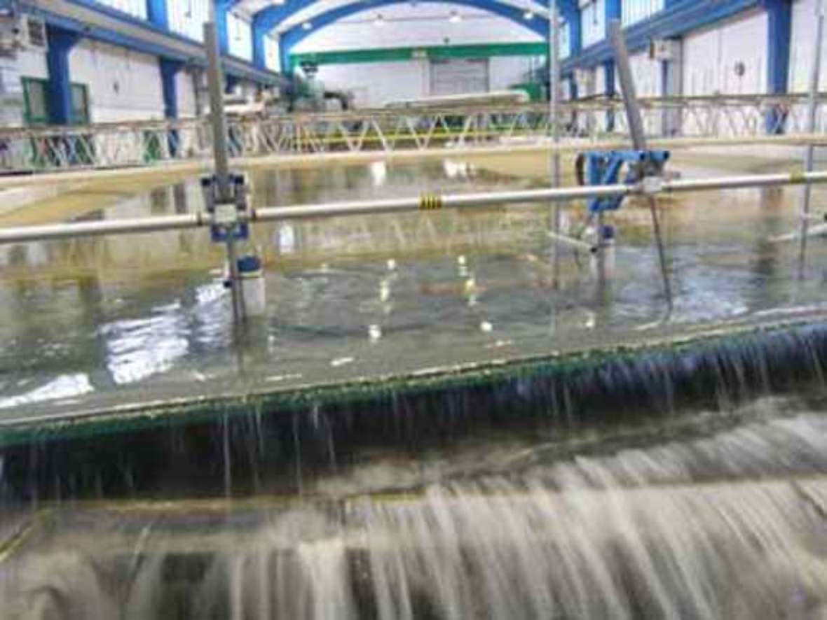 Man sieht wie Wasser über eine Kante nach unten fließt. Diese Kante ist Teil einer in der Höhe verstellbaren Klappe um den Wasserstand am unteren Ende des Modells in Abhängigkeit vom Durchfluss richtig einzustellen.