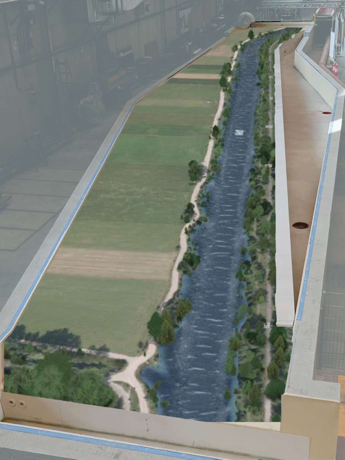 Man sieht eine ca. 30 Meter lange und 5 Meter breite Fläche, die mit ca. 1 Meter hohen Mauern umgeben ist. In diesem Bereich ist eine Visualisierung der Gail mit dem zukünftigen Aufweitungsbereich dargestellt. So sieht man wie das maßstäblich verkleinerte Modell der Gail in die Versuchsfläche passt.