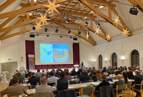 You can see the participants sitting at the back of the fishing conference at Mondsee Castle. On the stage is a large screen on which a presentation is being shown.