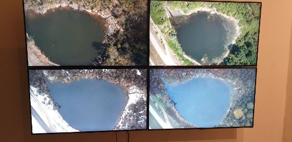Auf vier Bildschirmen sieht man aus der Vogelperspektive einen kleinen Teich im Augebiet der Donau. Jeder Bildschirm zeigt diesen Teich zu einer anderen Jahreszeit.